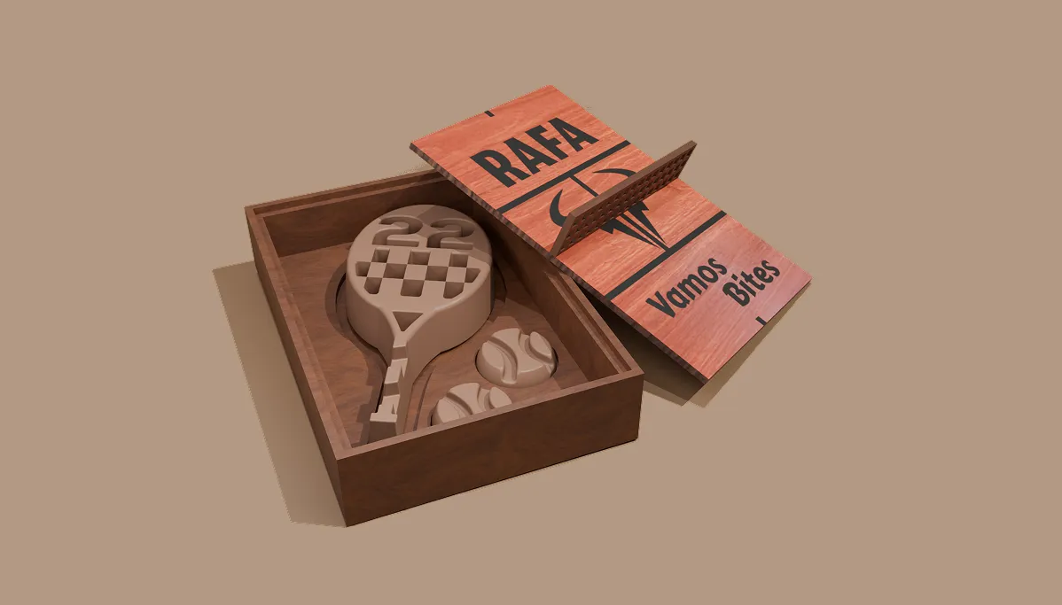 A walnut timber box opens to reveal a chocolate tennis racquet with a raised 22 and two chocolate ball coins, set against a peach clay-court backdrop.